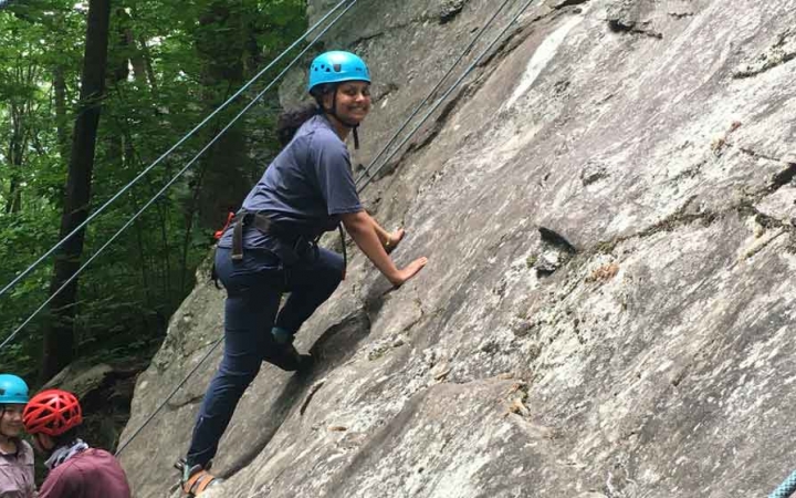 a gap year student pauses to smile at the camera while rock climbing on an outward bound course